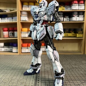 May include: A detailed, articulated model robot in white, gray, and black, with red accents. The model has a complex design with multiple panels and joints. The text "ArrowModelBuild" is visible in the top right corner.