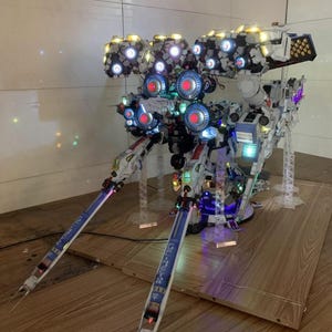 May include: A detailed model of a futuristic robot with multiple light-up components. The model features white, blue, and red accents, with the text "ArrowModelBuild" visible. The robot is displayed on a wooden surface.