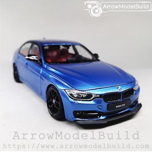 May include: A blue BMW 335i model car with black wheels and a black front spoiler. The model has red interior and the text "BMW 335i" is visible on the front. The image also includes the text "ArrowModelBuild".