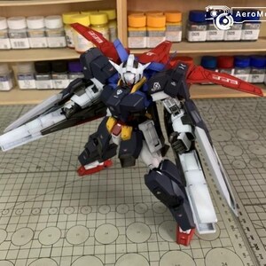 Puede incluir: Maqueta detallada de un robot mecha, con una combinaci&oacute;n de colores azul marino, blanco, rojo y amarillo. El robot tiene grandes alas y est&aacute; posado sobre una esterilla de corte. El logotipo de AeroModelBuild es visible en el fondo.