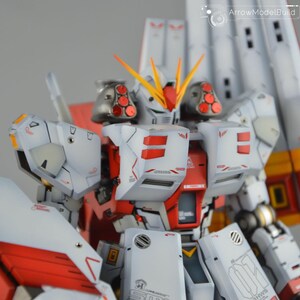 May include: A detailed model of a white and red mecha robot with yellow and orange accents. The robot has multiple panels, vents, and intricate details. The model is a close-up shot, showcasing the craftsmanship and design.