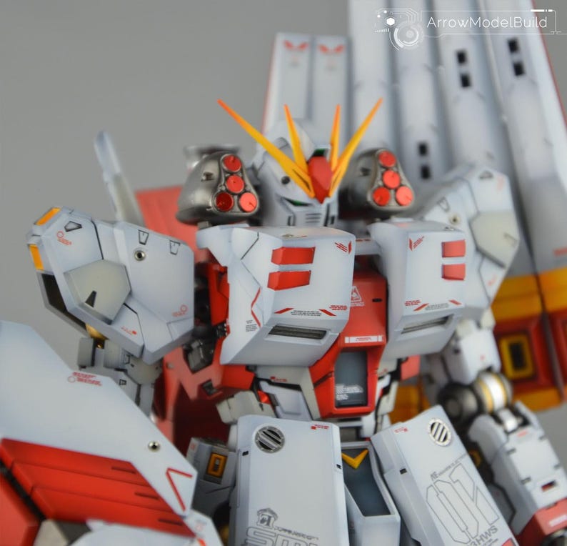 May include: A detailed model of a white and red mecha robot with yellow and orange accents. The robot has multiple panels, vents, and intricate details. The model is a close-up shot, showcasing the craftsmanship and design.