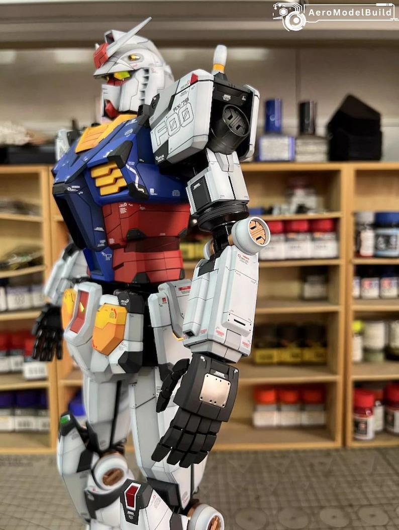 May include: A detailed model of a Gundam robot, featuring a white, blue, red, and yellow color scheme. The robot has intricate mechanical details, including segmented armor, articulated limbs, and a distinctive head with a V-fin. The model is posed in a dynamic stance.