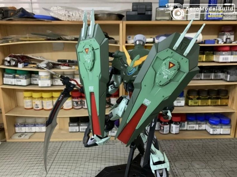 Puede incluir: Kit de modelo detallado de un robot Gundam, con una combinaci&oacute;n de colores verde y rojo. El robot tiene escudos grandes y angulares y una cuchilla curva. El modelo se exhibe frente a una estanter&iacute;a llena de pinturas y herramientas.