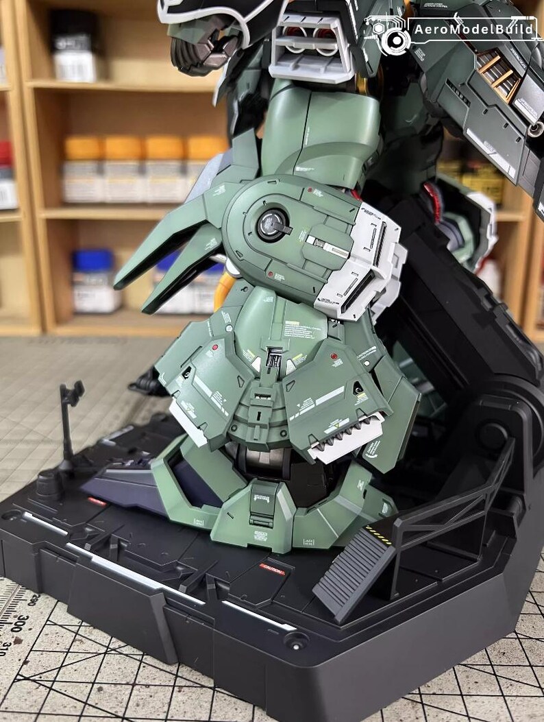 May include: A detailed, assembled model kit of a green and white mech robot. The model is on a black base with intricate panel lines and mechanical details. The image shows the robot's leg and lower torso.