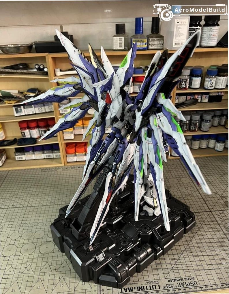 May include: A detailed model of a futuristic robot with large, wing-like structures. The model features a colour scheme of white, blue, and green accents, mounted on a black base. The model is a detailed representation of a science fiction or anime-inspired design.