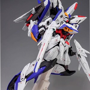 Puede incluir: Kit de modelo detallado de un robot futurista, predominantemente blanco con detalles en azul, rojo y negro. El modelo presenta extremidades articuladas, alas y l&iacute;neas de paneles intrincadas, montado sobre un soporte blanco. El texto "AeroModelBuild" es visible.