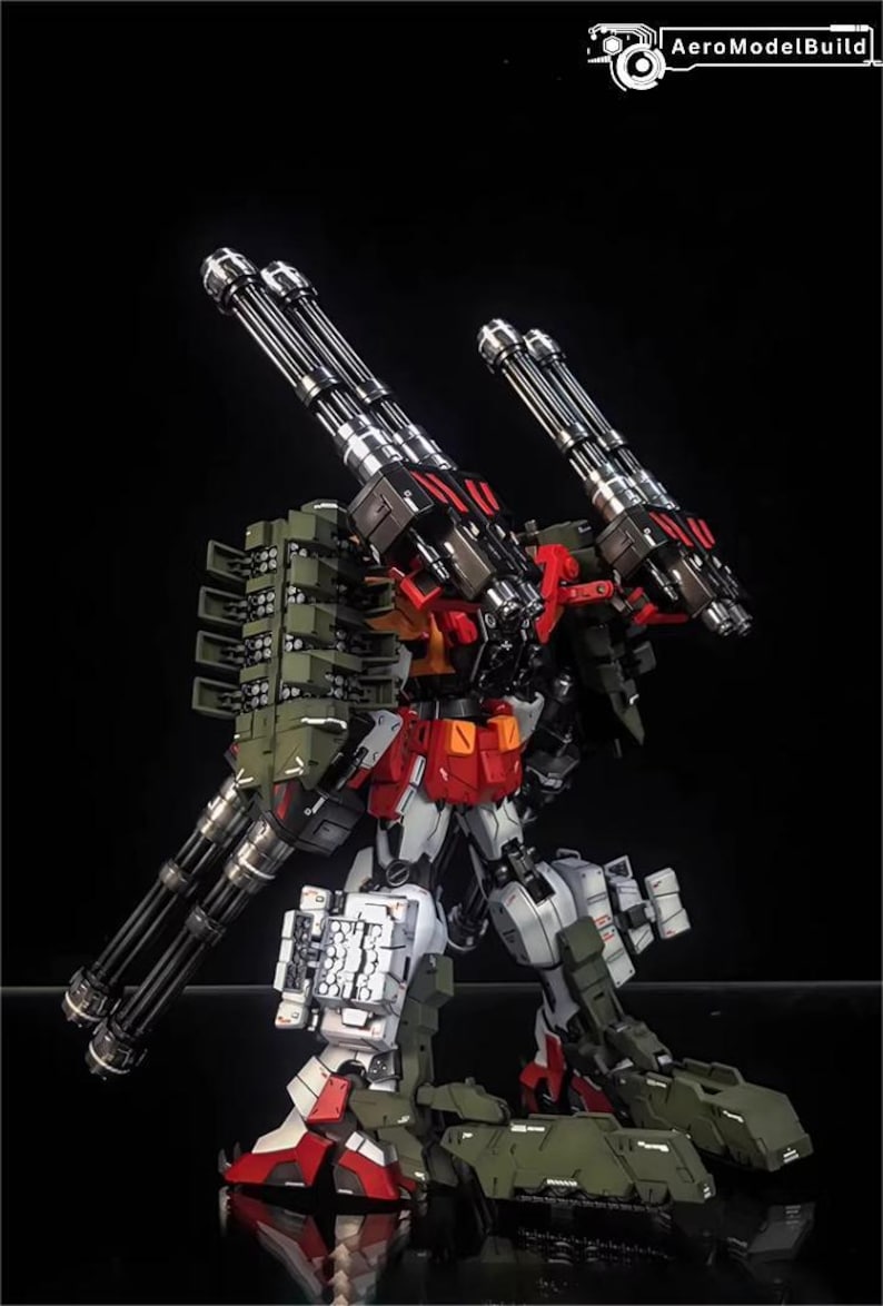 May include: A detailed model of a mech robot with multiple gun barrels and missile launchers. The robot is primarily white, red, and green, with silver gun barrels. The AeroModelBuild logo is in the top right corner.