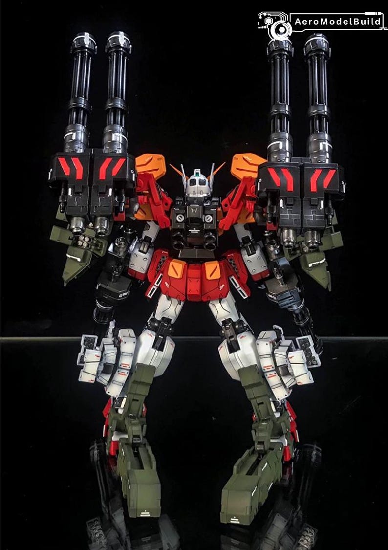K&ouml;nnte beinhalten: Eine mehrfarbige Roboter-Actionfigur mit zwei gro&szlig;en schwarzen Gatling-Kanonen an den Schultern, rot-wei&szlig;er Panzerung und olivgr&uuml;nen Beinkomponenten. Der Text AeroModelBuild ist in der oberen rechten Ecke des Bildes zu sehen.