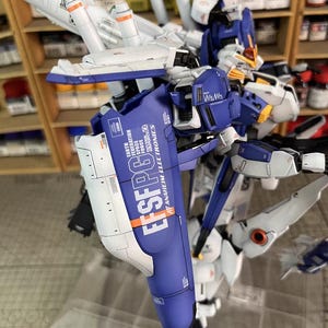 May include: A detailed model of a futuristic robot, predominantly blue, white, and grey. The model features intricate mechanical details, including wings and articulated limbs. Text on the model reads "EFSFPG6" and "ANAHEIM ELECTRONICS".