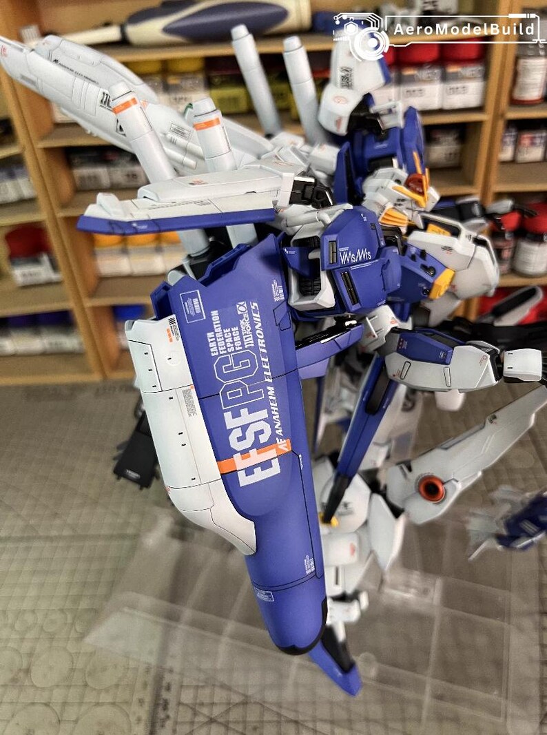 May include: A detailed model of a futuristic robot, predominantly blue, white, and grey. The model features intricate mechanical details, including wings and articulated limbs. Text on the model reads "EFSFPG6" and "ANAHEIM ELECTRONICS".