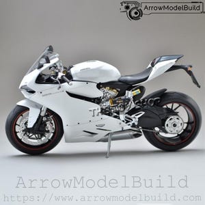 Peut inclure: Maquette de moto Ducati blanche avec des détails noirs et rouges. Le modèle présente des composants de moteur détaillés et un design épuré. Le texte "ArrowModelBuild" et une adresse de site Web sont inclus.