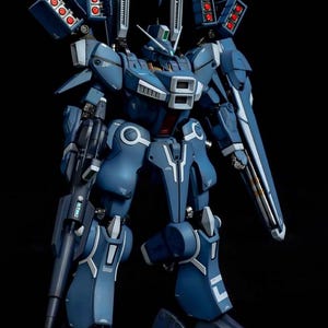 May include: A detailed model of a blue and white mech robot with multiple weapon systems. The robot has a complex design with visible mechanical components, including missile launchers and a large shield. The AeroModelBuild logo is in the top right corner.