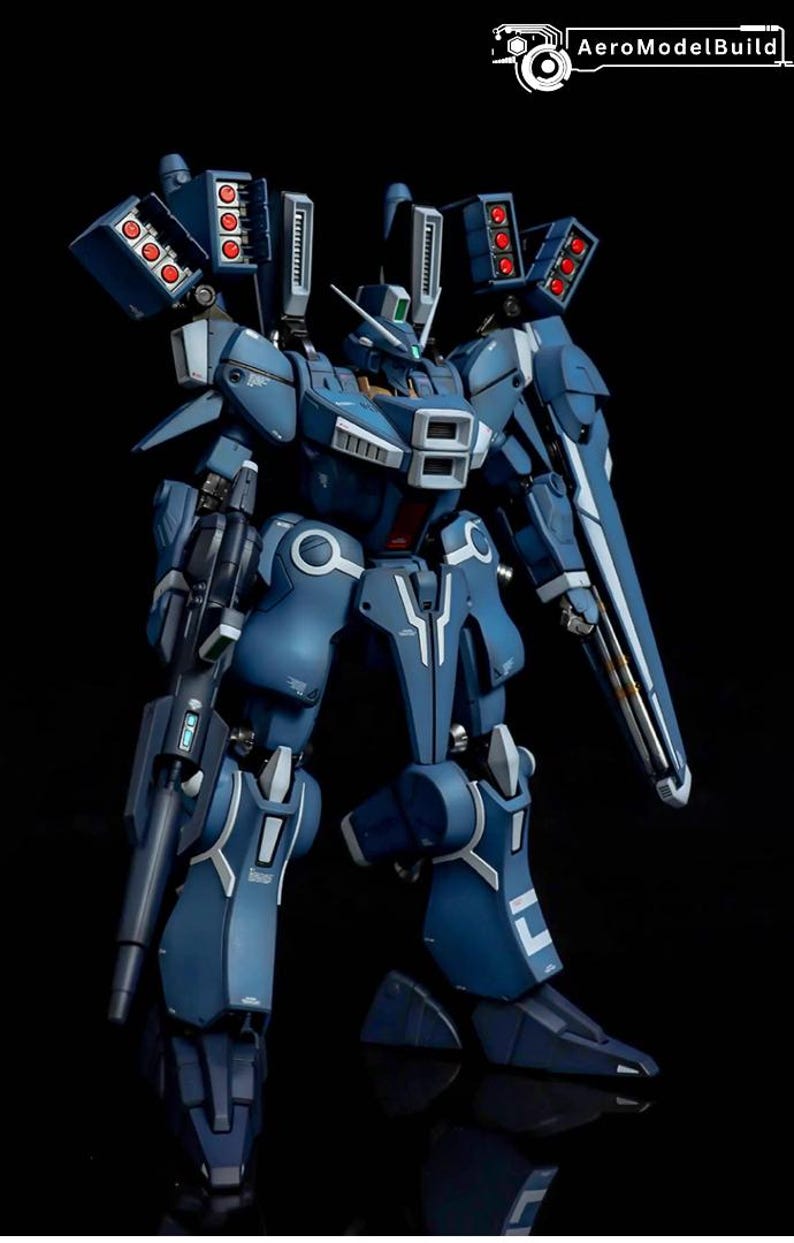 May include: A detailed model of a blue and white mech robot with multiple weapon systems. The robot has a complex design with visible mechanical components, including missile launchers and a large shield. The AeroModelBuild logo is in the top right corner.