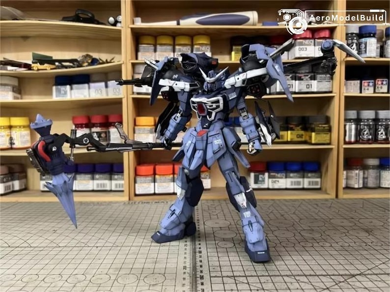 May include: A detailed model of a blue and gray mech robot with articulated limbs and weapons. The robot has a complex design with multiple panels, wings, and a detailed head. The background shows shelves filled with model-building supplies.