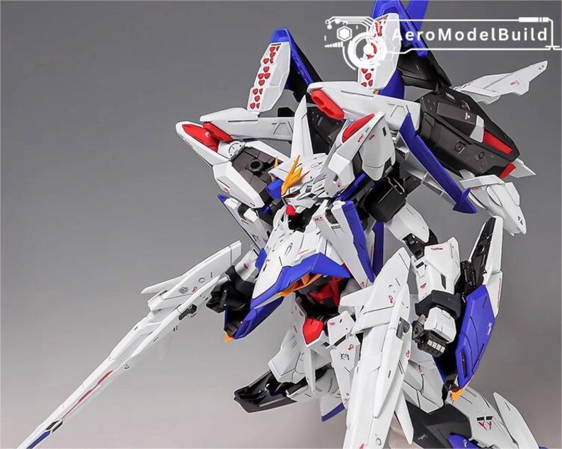 Puede incluir: Modelo detallado de un robot mecha blanco, azul y rojo con una gran espada. El modelo tiene detalles intrincados, incluyendo acentos en forma de coraz&oacute;n y el texto "AeroModelBuild". El robot est&aacute; posado din&aacute;micamente sobre un fondo gris.