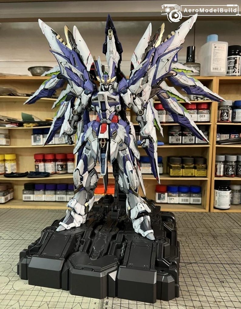 May include: A highly detailed model robot, featuring a colour scheme of white, blue, and red, positioned on a black platform. The robot has large, wing-like structures. The image includes the text "AeroModelBuild" in the upper right corner.