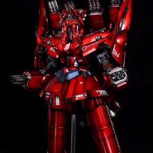 May include: A detailed, red model of a mecha robot with multiple weapons and armor plating. The model is standing on a black base with a silver support stand. The robot has a complex design with various mechanical components.