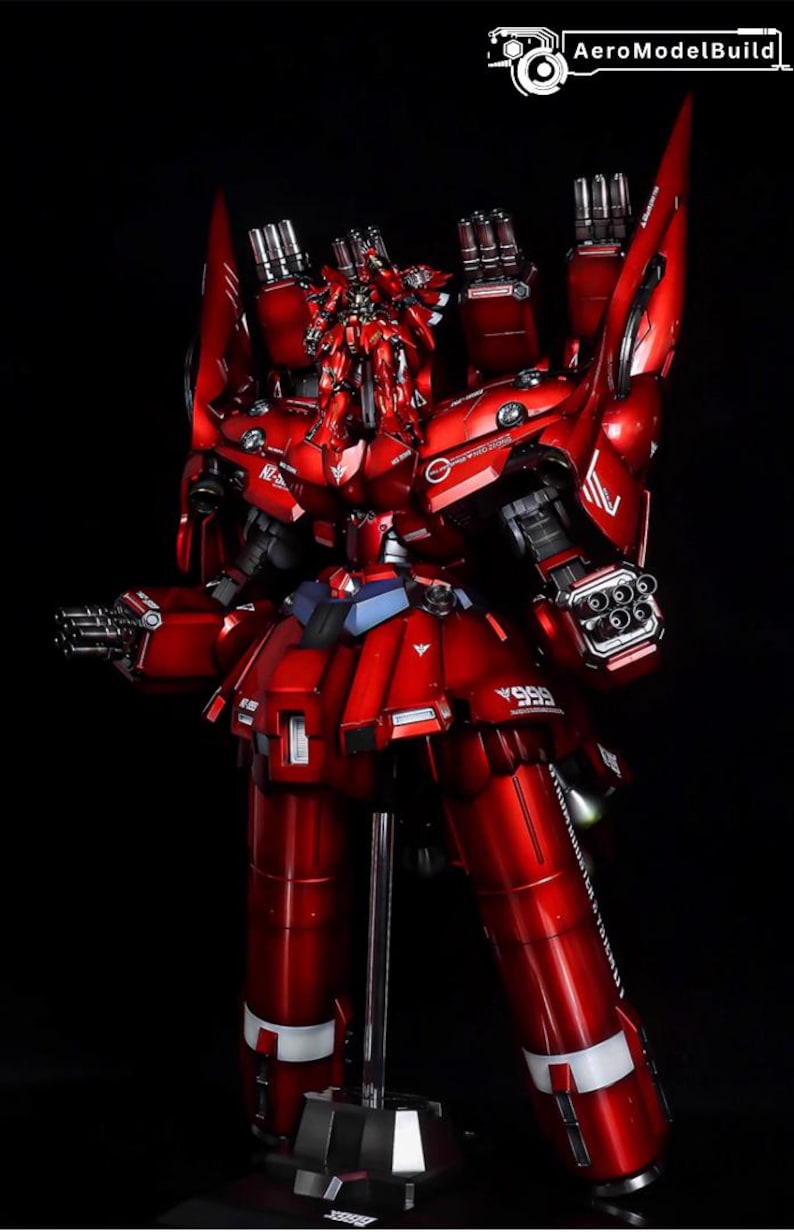 May include: A detailed, red model of a mecha robot with multiple weapons and armor plating. The model is standing on a black base with a silver support stand. The robot has a complex design with various mechanical components.