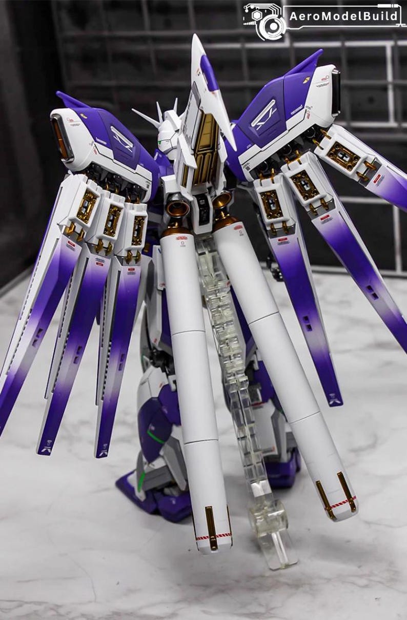 May include: A detailed model kit of a futuristic robot, featuring a color scheme of white, purple, and gold. The model has multiple articulated wings and a clear stand. The text "AeroModelBuild" is visible.