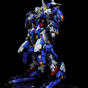 May include: A detailed model of a blue, white, and yellow mecha robot with sharp angles and intricate details. The robot stands on a black base, with red accents on the feet and a green head. The AeroModelBuild logo is in the top right corner.