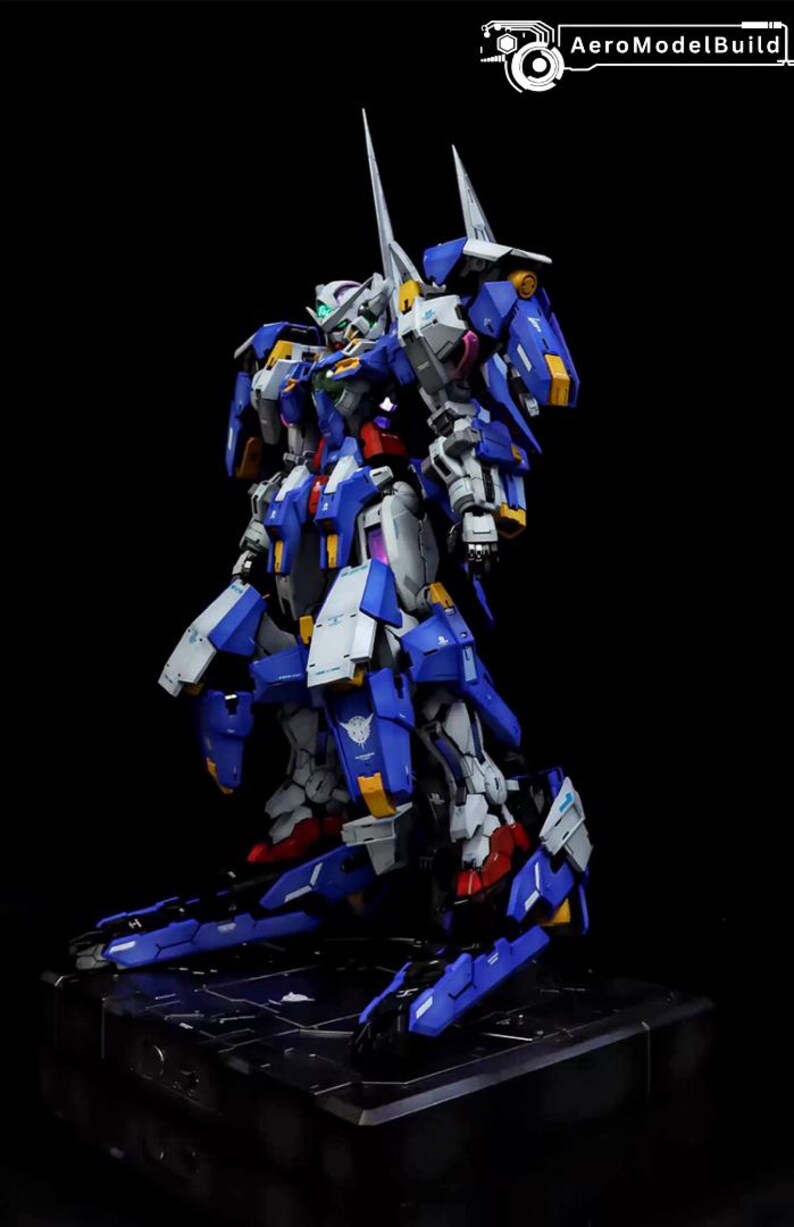 May include: A detailed model of a blue, white, and yellow mecha robot with sharp angles and intricate details. The robot stands on a black base, with red accents on the feet and a green head. The AeroModelBuild logo is in the top right corner.