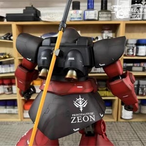 May include: A detailed model of a red and black mecha robot with an orange pole. The robot has a black torso with the text "PRINCIPALITY OF ZEON". The background shows shelves with paint bottles.