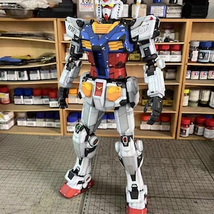 May include: A detailed model of a Gundam robot, primarily white with blue, red, and yellow accents. The model has intricate panel lines and is posed upright. The image includes the text "EFSF" and "F00".