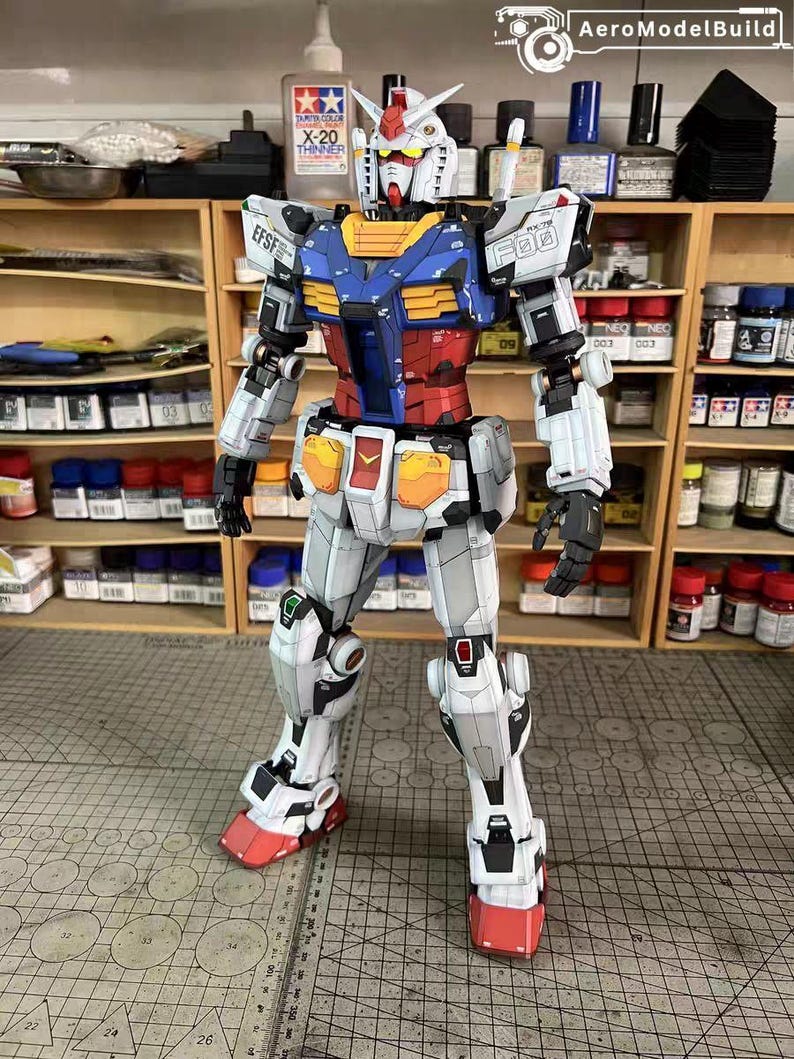 May include: A detailed model of a Gundam robot, primarily white with blue, red, and yellow accents. The model has intricate panel lines and is posed upright. The image includes the text "EFSF" and "F00".