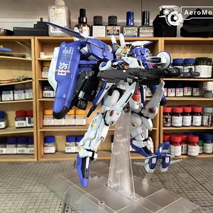 May include: A detailed model robot, mainly white and blue, holding a large weapon. The model is displayed on a clear stand. The text "EFSF PG" is visible on its back. Shelves with bottles and containers are in the background.