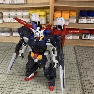 Puede incluir: Kit de modelo detallado de un robot mecha, con una combinaci&oacute;n de colores azul marino, blanco, rojo y amarillo. El robot tiene grandes alas y est&aacute; equipado con dos espadas largas y blancas. El modelo est&aacute; posado sobre una esterilla de corte.