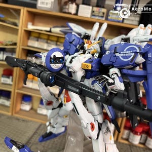 May include: A detailed model robot in blue, white, and yellow, holding a black rifle. The robot features a shield with the text "110 TASK FORCE" and "EARTH FEDERATION SPACE FORCE". The model is set against a background of shelves.