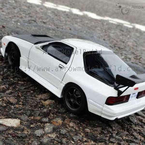 Könnte beinhalten: Ein weißes Modellauto mit schwarzer Motorhaube und Spoiler, geparkt auf einer strukturierten Oberfläche. Das Auto hat schwarze Räder und ein Nummernschild. Das Bild enthält den Text "ArrowModelBuild" und eine Website-Adresse.