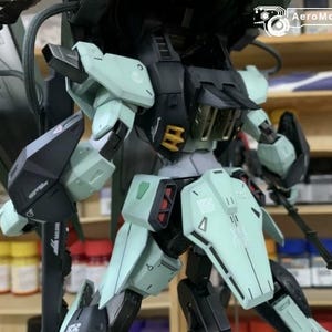 Puede incluir: Maqueta detallada de un robot mec&aacute;nico, con una combinaci&oacute;n de colores negro, verde menta y detalles en rojo. El robot tiene extremidades articuladas y detalles intrincados en los paneles. El logo AeroModelBuild es visible.