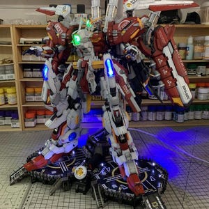 Puede incluir: Un modelo detallado de robot con armadura roja, blanca y gris, iluminado con luces azules y verdes. El modelo est&aacute; sobre una plataforma negra con un dise&ntilde;o geom&eacute;trico. Los textos "0033" y "PME" son visibles en el modelo. El texto "ArrowModelBuild" tambi&eacute;n es visible.