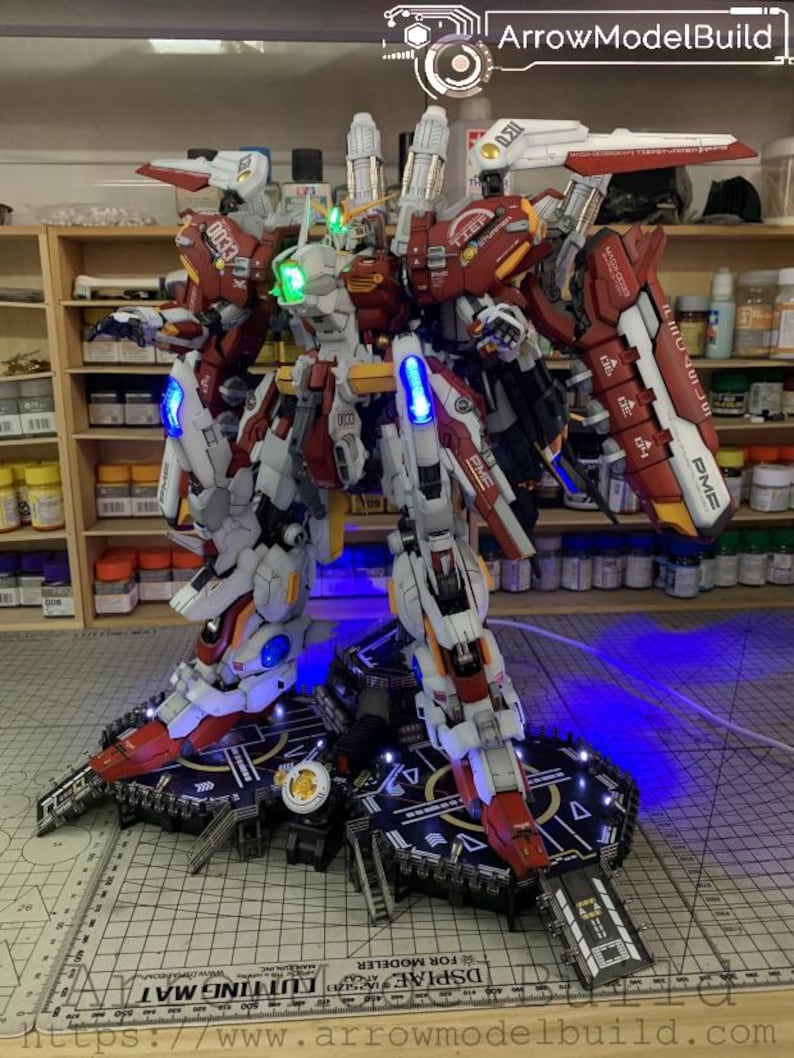 Puede incluir: Un modelo detallado de robot con armadura roja, blanca y gris, iluminado con luces azules y verdes. El modelo est&aacute; sobre una plataforma negra con un dise&ntilde;o geom&eacute;trico. Los textos "0033" y "PME" son visibles en el modelo. El texto "ArrowModelBuild" tambi&eacute;n es visible.