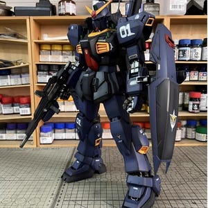 Pu&ograve; includere: Modello dettagliato di un robot mecha blu scuro e nero con accenti arancioni e gialli. Il robot ha un grande scudo e un fucile. Il numero "01" &egrave; visibile sulla spalla e sulla gamba. Il modello &egrave; ambientato su uno sfondo di barattoli di vernice e scaffali.