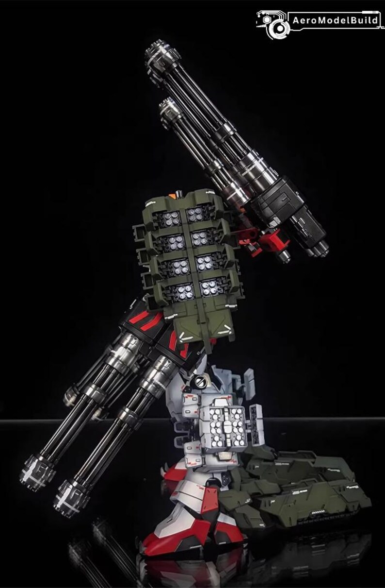 May include: AeroModelBuild model kit of a detailed robot with multiple parts. The model features silver, black, red, white, and green components, including large cannons and missile launchers. The logo "AeroModelBuild" is visible on the image.