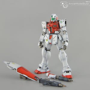 Puede incluir: Un modelo de robot blanco y rojo con accesorios desmontados. El robot tiene un pecho y detalles de la cabeza rojos, con el número "23" en los hombros y las piernas. Incluye un escudo rojo y blanco, una pistola y un arma más pequeña.