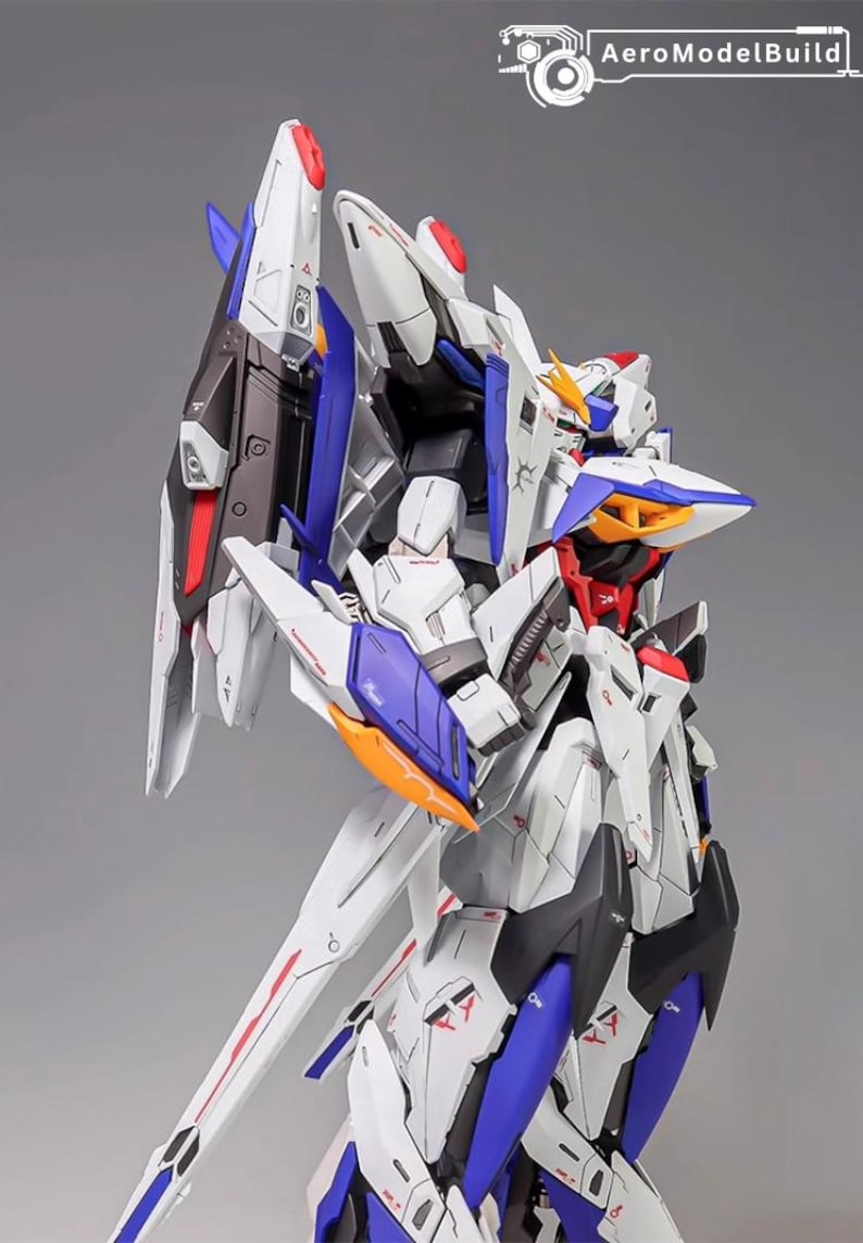 Puede incluir: Maqueta detallada de un robot futurista, principalmente blanco con detalles azules, rojos y naranjas. El modelo presenta paneles intrincados y &aacute;ngulos agudos, con una gran estructura en forma de ala en la espalda. El logotipo de AeroModelBuild es visible.