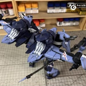 May include: A detailed model of a futuristic aircraft, primarily in shades of blue and gray, with intricate mechanical details. The model features wings, a cockpit, and various weapon-like attachments. The background includes shelves with paint bottles.