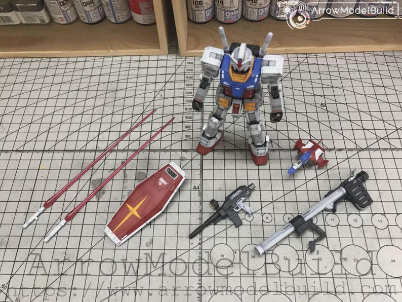 以下が含まれることがあります： 白、青、赤、黄色の配色が特徴のガンダムロボットの精密模型キット。 シールド、武器、長い赤い槍などの様々なアクセサリーが含まれています。 モデルはグリッドパターンの表面に配置されています。