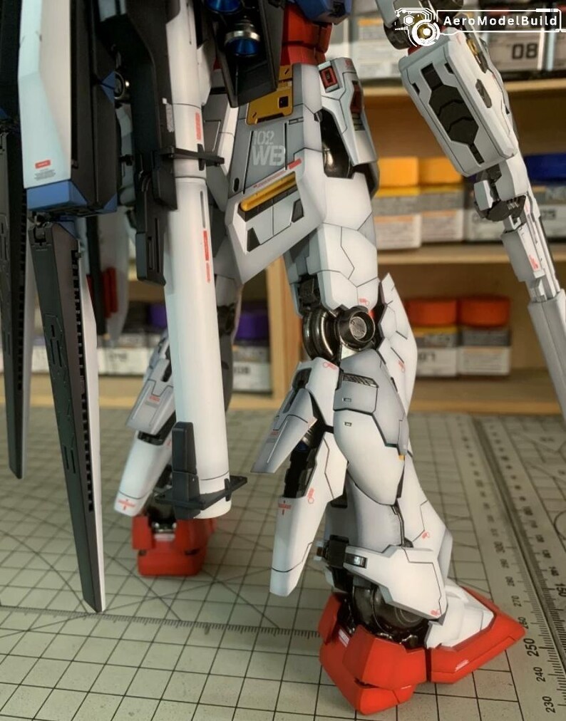K&ouml;nnte beinhalten: Detaillierter, teilmontierter Modellbausatz eines Mech-Roboters. Das Modell hat wei&szlig;e, graue, rote und schwarze Komponenten. Der Text "102 WB" ist auf dem Bein sichtbar. Das Modell steht auf einer Rasteroberfl&auml;che.