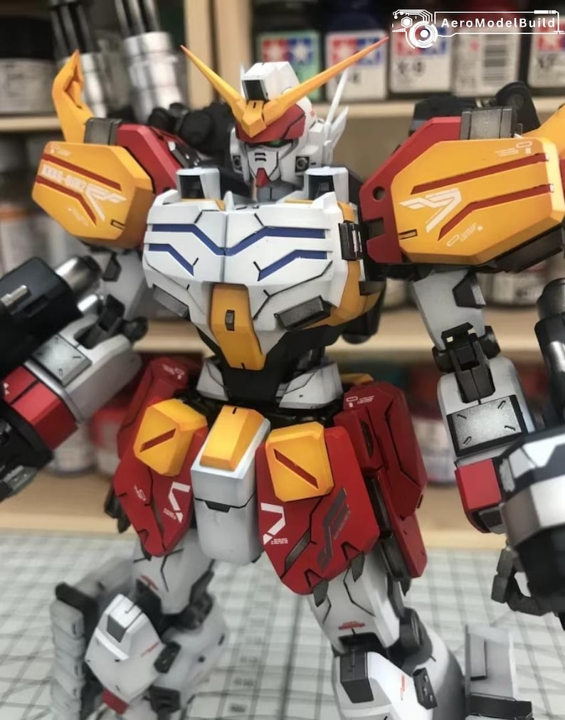 K&ouml;nnte beinhalten: Detailliertes Modell eines Gundam-Roboters mit einer Farbgebung aus Wei&szlig;, Gelb, Rot und Grau. Der Roboter hat komplizierte Linien und Markierungen, mit scharfen Winkeln und einer dynamischen Pose. Das Modell ist ein Sammlerst&uuml;ck.