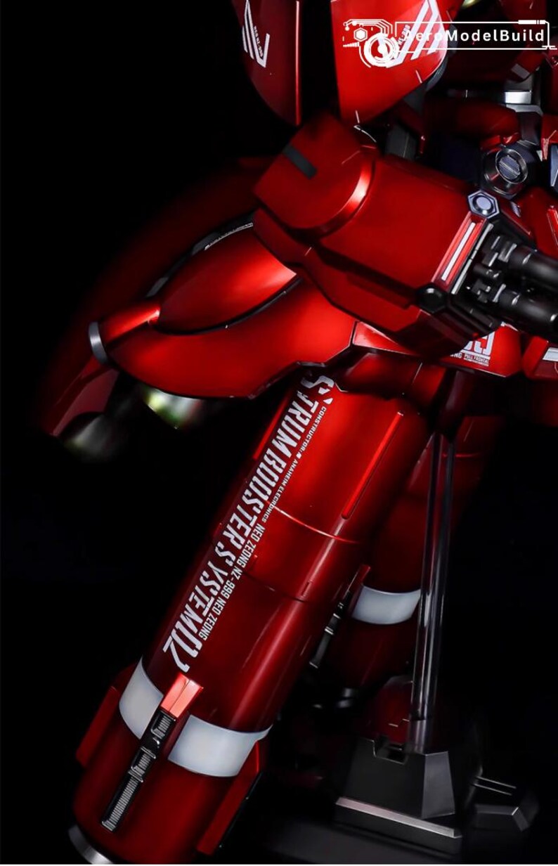 May include: A detailed, red model kit of a mobile suit, featuring metallic accents and intricate mechanical details. The model has the text "STRUM BOOSTER SYSTEM" and "ModelBuild" on it. The kit is displayed against a black background.