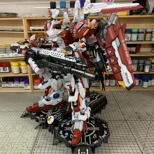 Puede incluir: Un modelo detallado de un robot mecha, principalmente blanco y rojo, con detalles en negro y gris. El robot est&aacute; de pie sobre una plataforma negra con un dise&ntilde;o complejo. La imagen incluye el texto "ArrowModelBuild" y "DSPLA".