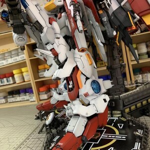 Puede incluir: Modelo detallado y ensamblado de un robot con armadura blanca, roja y gris. El modelo presenta intrincados detalles mec&aacute;nicos, incluyendo articulaciones y accesorios de armas. El robot est&aacute; posado sobre una plataforma negra con marcas blancas.