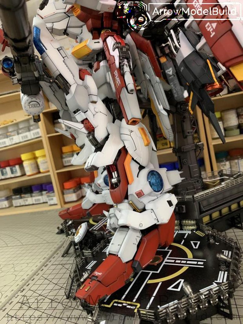 Puede incluir: Modelo detallado y ensamblado de un robot con armadura blanca, roja y gris. El modelo presenta intrincados detalles mec&aacute;nicos, incluyendo articulaciones y accesorios de armas. El robot est&aacute; posado sobre una plataforma negra con marcas blancas.