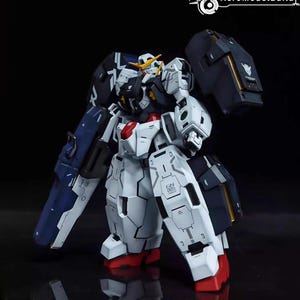 May include: A detailed model of a Gundam robot, primarily white with blue, black, red, and yellow accents. The robot has a complex design with multiple panels and articulated parts, standing on a reflective surface.