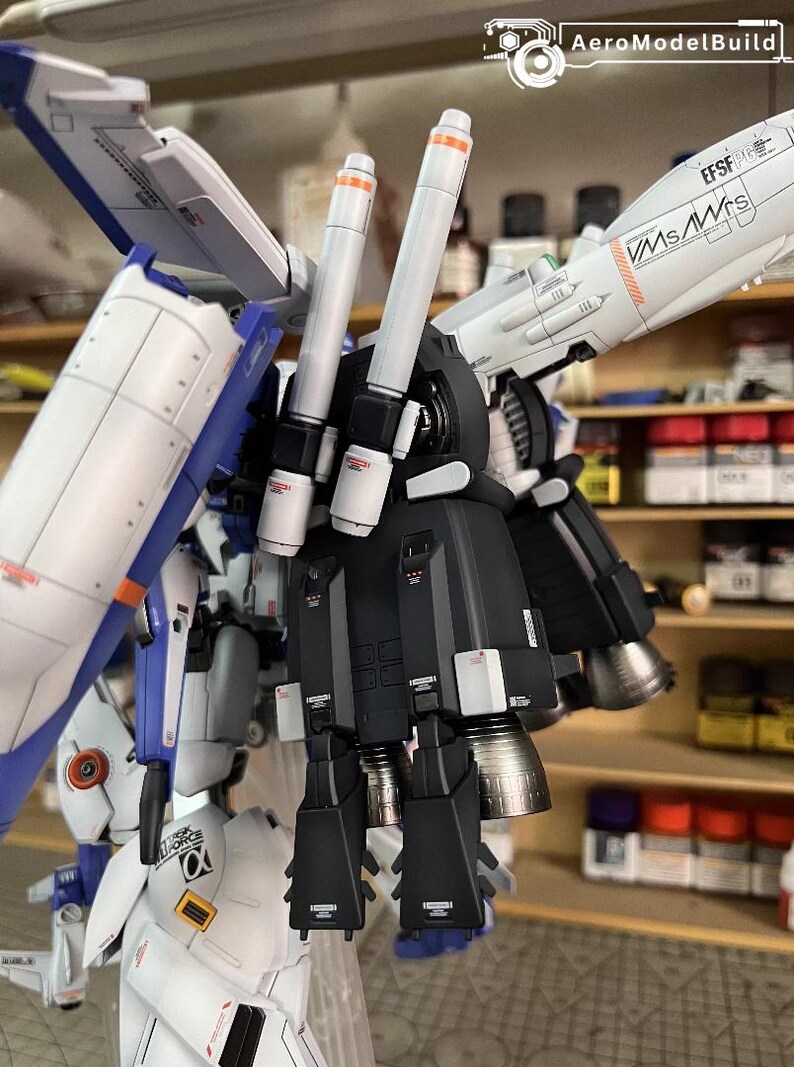 May include: A detailed model kit of a futuristic robot, featuring white, blue, and black armour with orange accents. The model has multiple thrusters and wings, with text that reads "EFSF" and "VMS/WrS". The AeroModelBuild logo is visible.